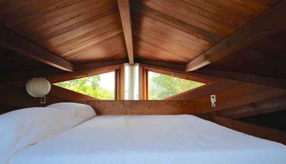 The interior of a bedroom with a white bed with a diamond shaped window and wood framed.