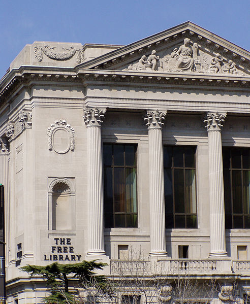 Detail of a Beaux-Arts style structure with the pediment and columns visible. The text "The Free Library" is in all capital, bronze letters on the lower left.