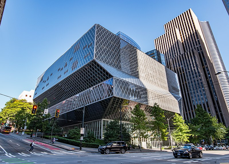 The Public Library in Seattle is shown from the corner. It rises in three layers, each layer hangs over the lower one a little more, so the effect is like an inverted pyramid. There is a diamond pattern on the facade made with steel beams, intersecting.