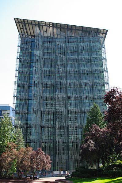 A glass and steel skyscraper seen from afar. The roofline is at a diagonal. The building has texture from vertical metal reeds that cover its facade.