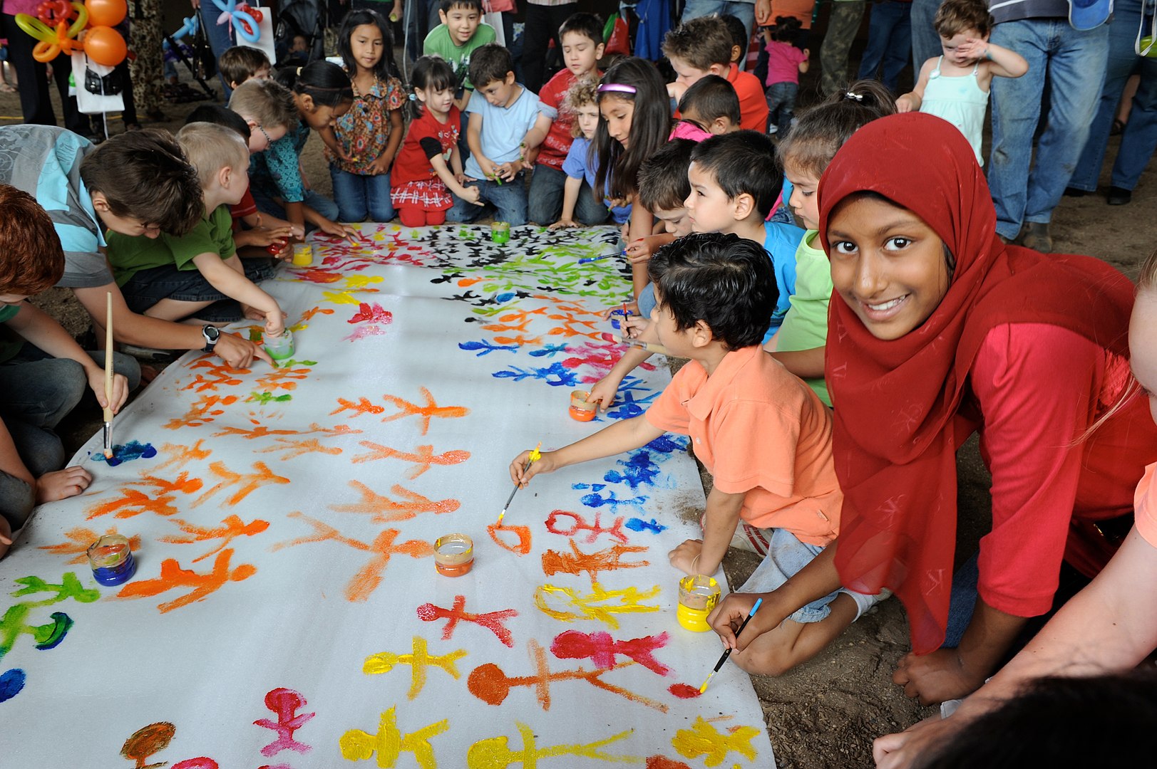 Photo of a group of young people from different cultures painting on a large piece of paper on the ground.