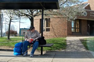 Photograph of a man sitting on a bench outside of a public building.