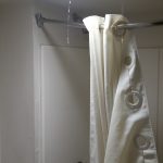 Photograph of a shower curtain in a shower with water dripping through a light fixture.