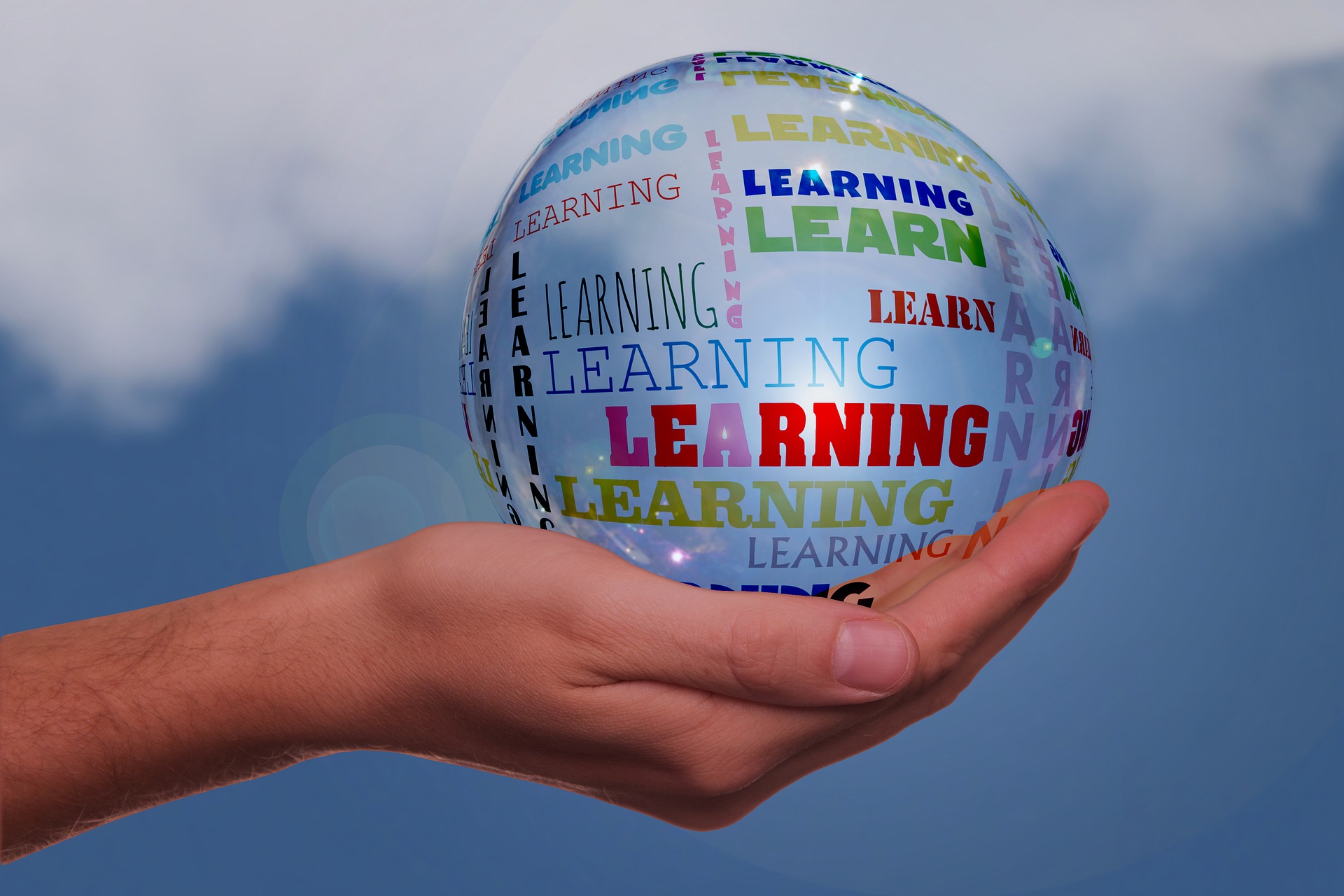 Photo of hand holding a clear ball with the words Learning all around it.