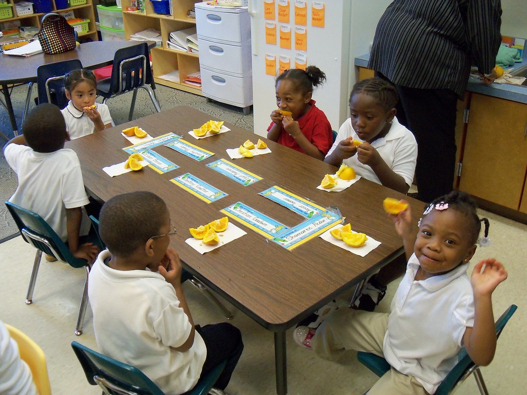 Six young children sitting around a table and eating orange slices