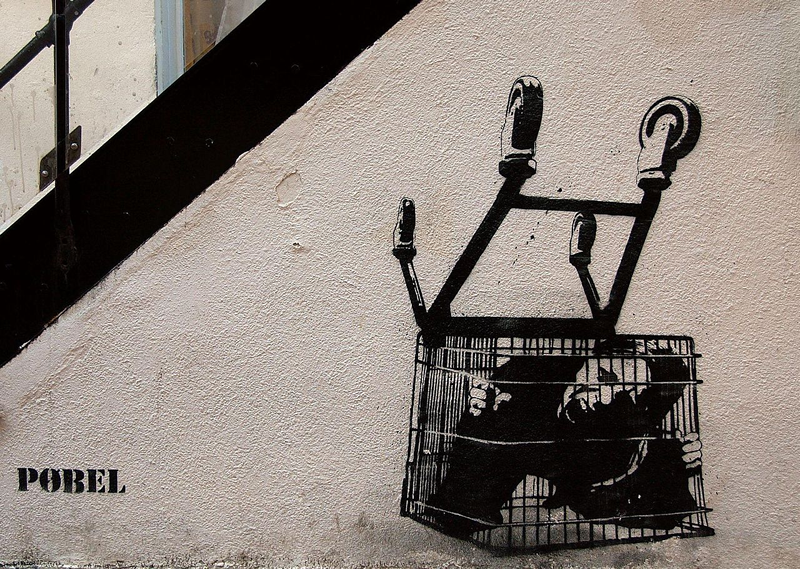 Graffiti depicting a screaming person trapped in the cage of an overturned shopping cart