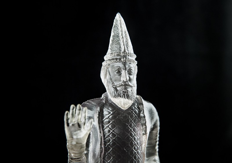 A translucent sculpture of a man with his right hand raised, palm facing out to the viewer.