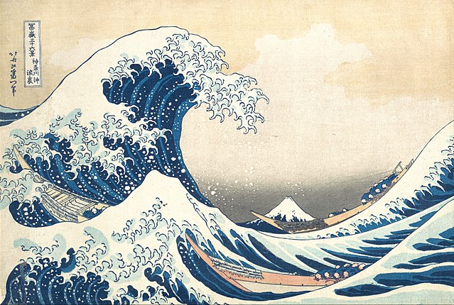 Multicolored woodcut print of a large wave curling up from the left side of the composition. In the distance is a mountain, Mt. Fuji with a white snowcap. In the wave is a boat with several passengers in the middle foreground and another boat the back right; both are moving with the wave.