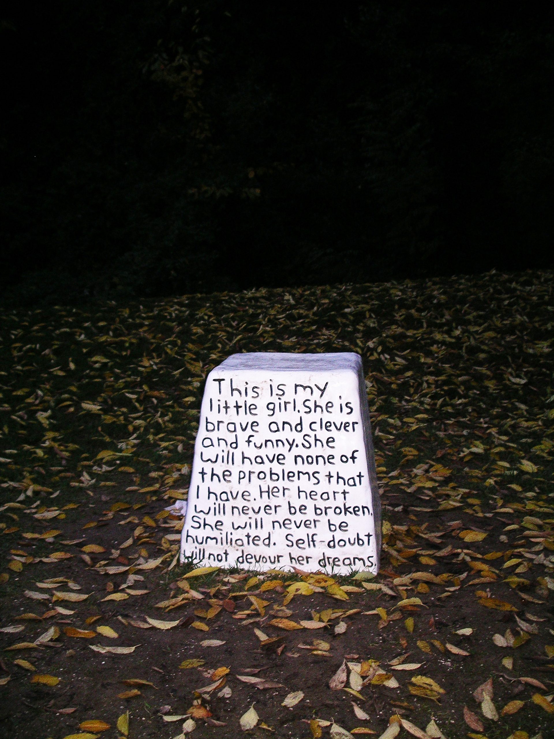 An empty pedestal in a landscape of leaves with words inscribed.