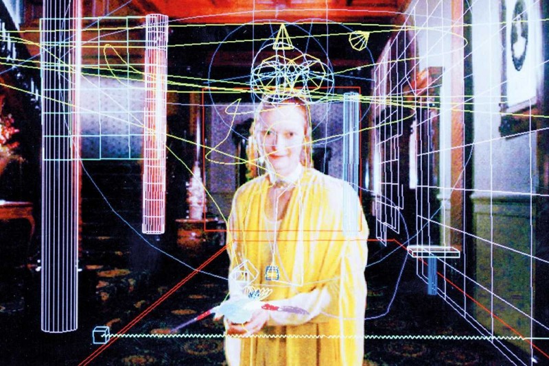 Screenshot from the film, Conceiving Ada. Actress Tilda Swinton as Ada Lovelace in a yellow dress and a room that looks like it is being generated in a computer simulation.