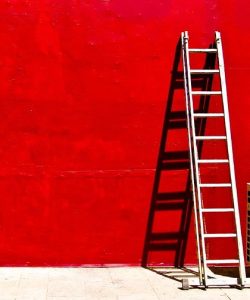 a white ladder leaning on a red wall, casting it shadow