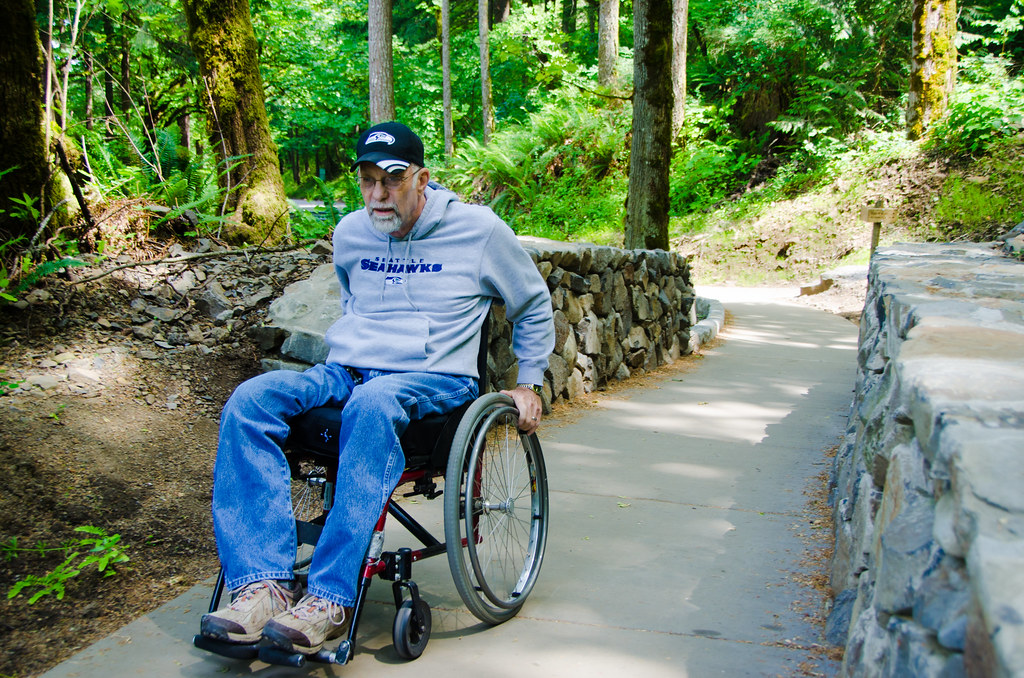 man with white beard in wheelchair on paved forest path