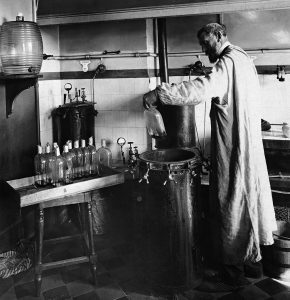 photo of an older Pasteur in a laboratory with stoppered flasks and a fermentation tank.