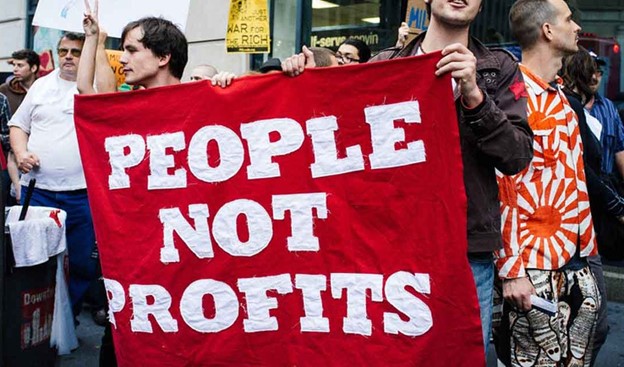 A photo of protestors holding a sign that reads 'people not profits'