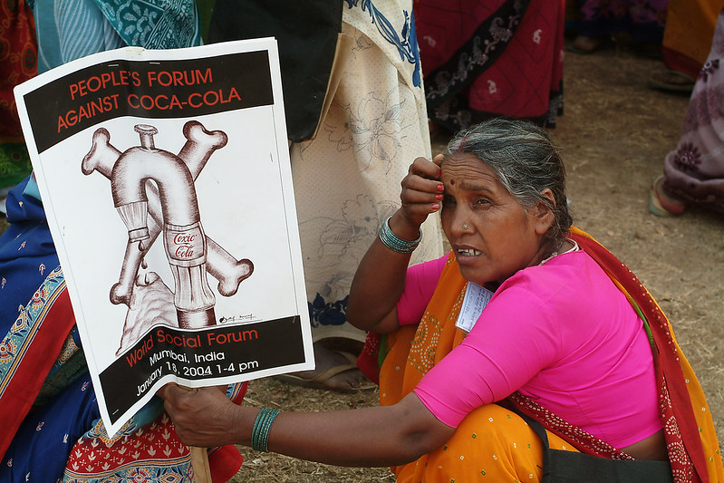An image of a woman in Mumbai holding a sign protesting Coca-Cola's control of water