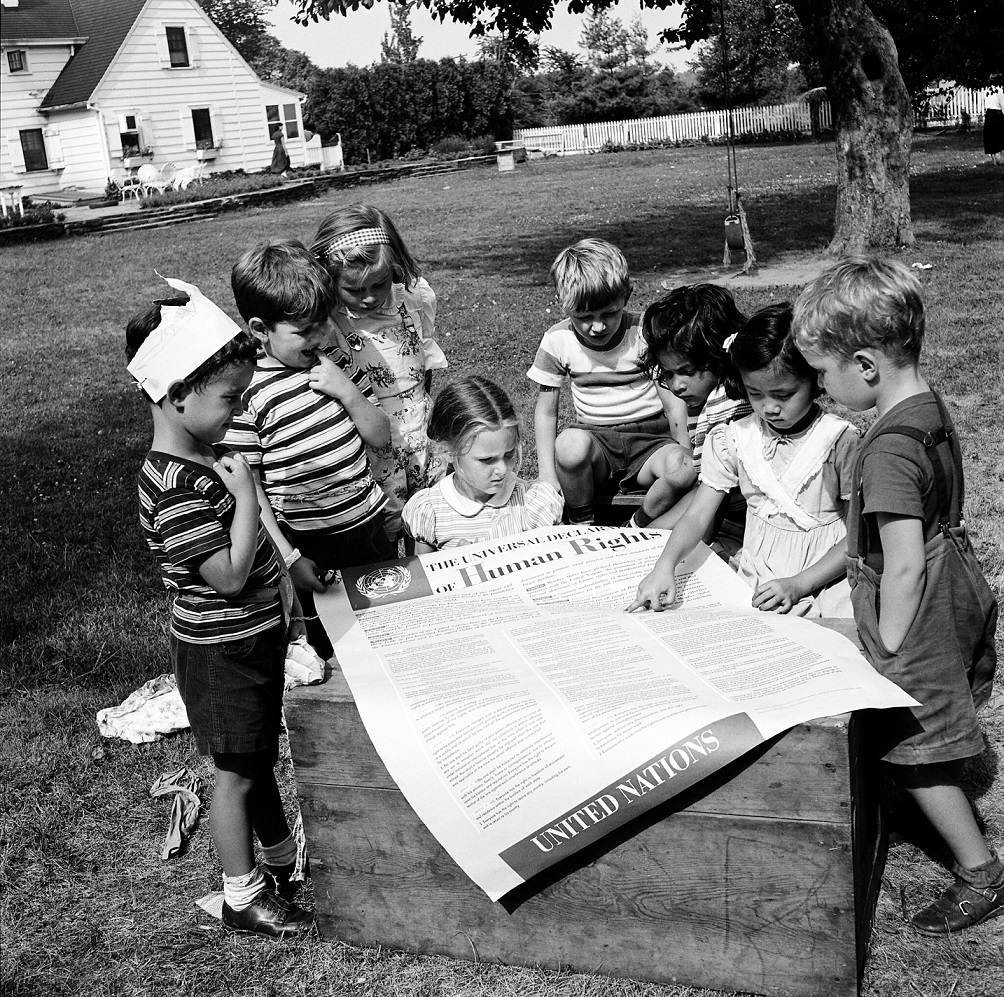 This is a photograph of children looking at a large print-out of the Universal Declaration of Human Rights.