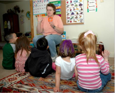 Woman sitting in chair with group of small children gathered around her