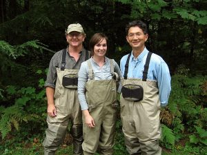 Three people wearing waders and posing in the woods.