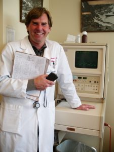 A smiling physician standing in front of medical equipment.