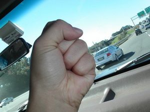 Someone holding their fist up in anger while driving on the freeway.