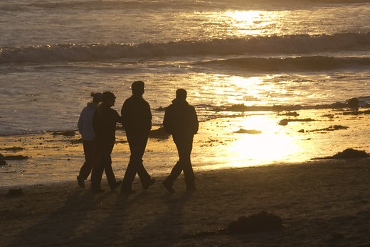 Four people walking down the beach together.