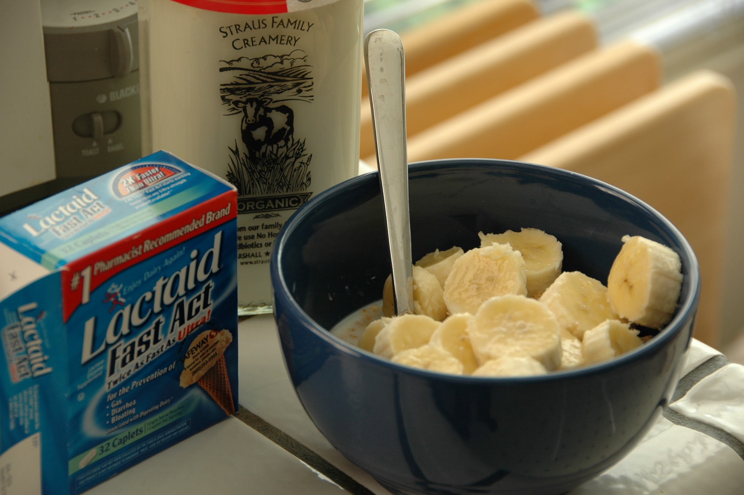 A photograph depicts a blue bowl of cereal, topped with sliced bananas. Behind it is a glass bottle of milk, and to the left is a box labeled "Lactaid: Fast Act."