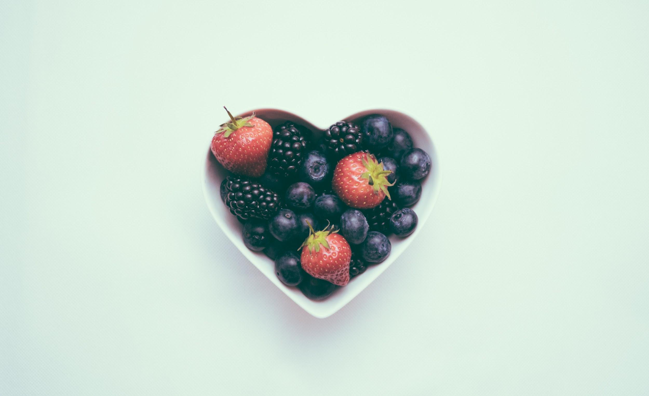 A white heart-shaped bowl filled with blackberries, blueberries, and strawberries