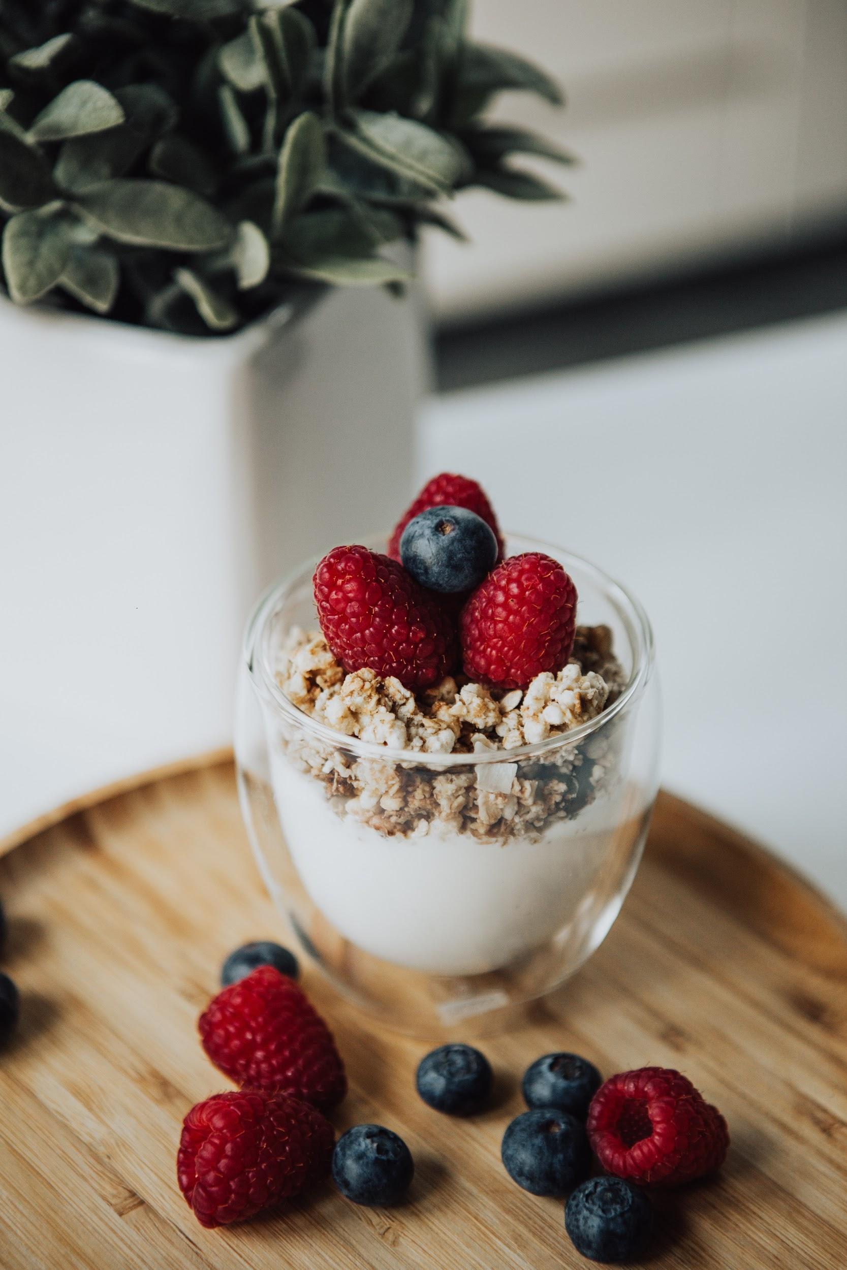 A yogurt parfait with granola and fresh berries in a clear glass is shown sitting on a table