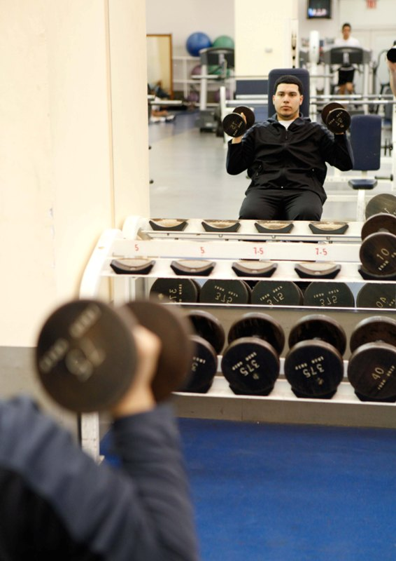 A man in a gym sitting on a bench with dumbbells in his hands.
