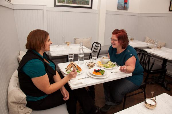 A picture showing two women with obesity eating lunch together. The women are laughing and enjoying their time together.