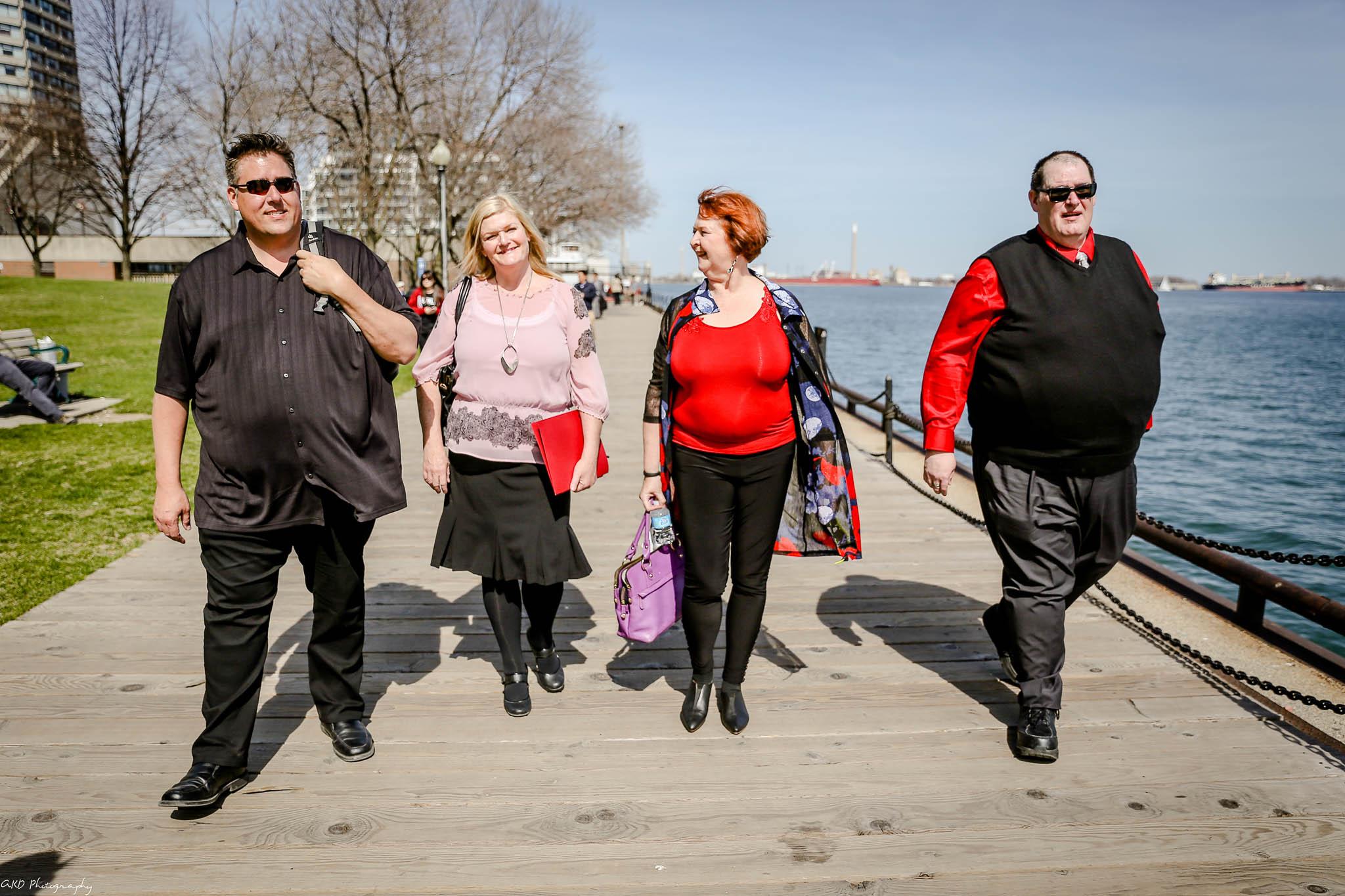 Two adult males and two adult females with obesity are walking outside, smiling and conversing with each other.