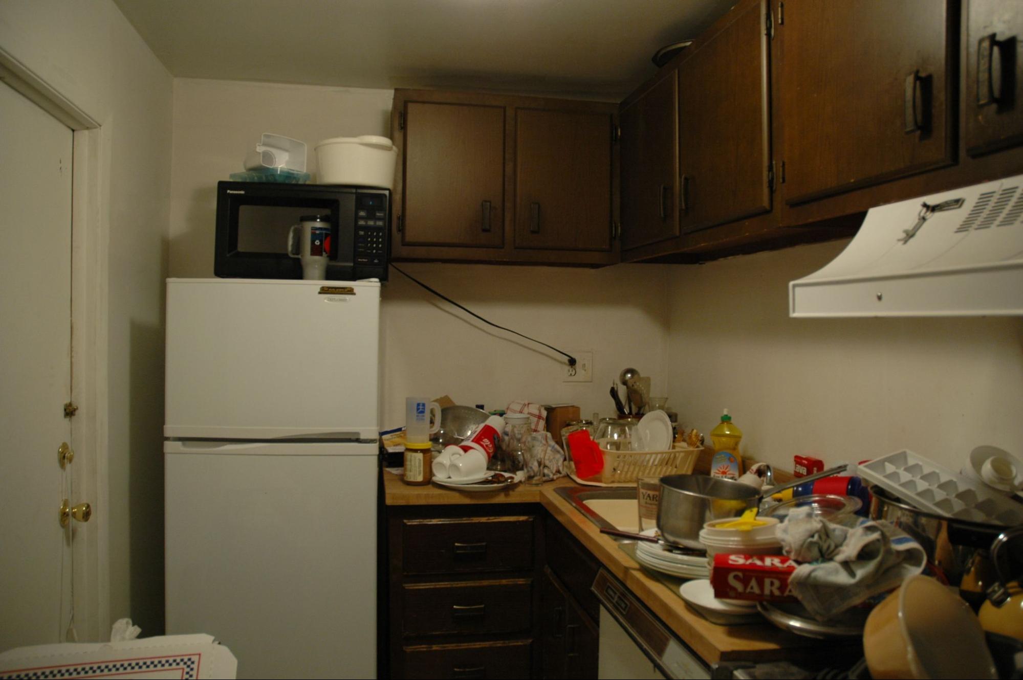 A kitchen with dishes covering the counter and in the sink, and small appliances stacked on the refrigerator.