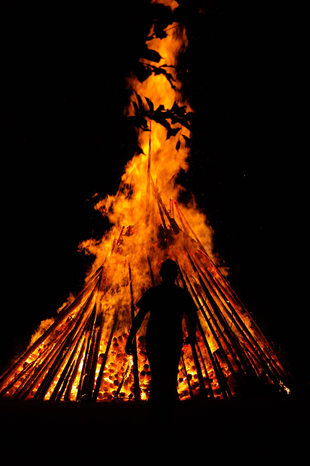 Shadow of a person walking away from a large pile of burning logs