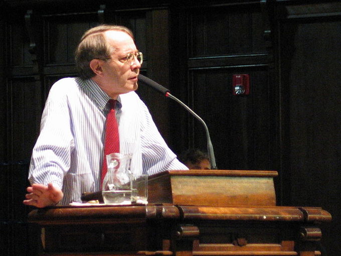 A White man leans over the podium and speaks into a microphone.