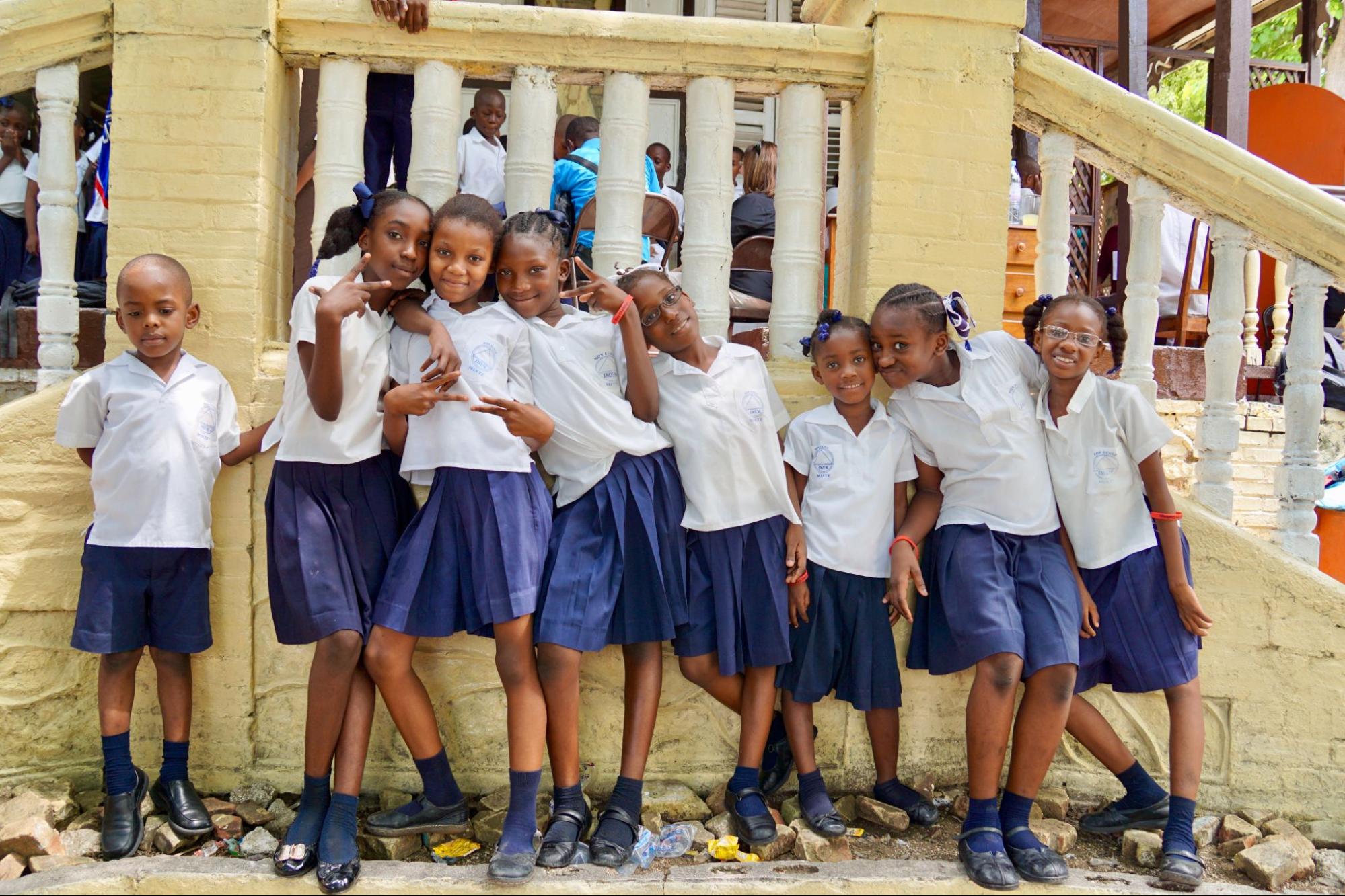 Seven young Black girls are posing together in a group, facing the camera and smiling.