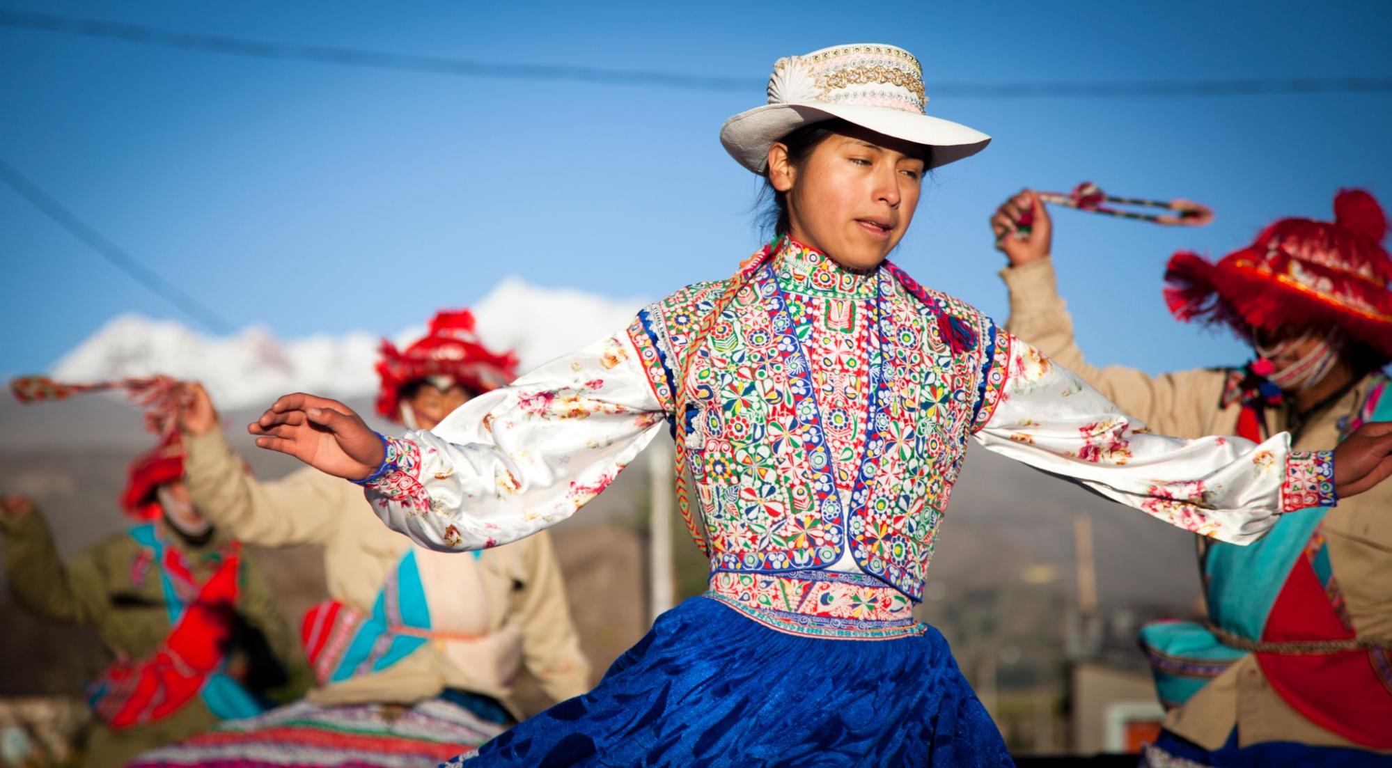 A female Peruvian dancer has arms raised to her sides in mid-dance.