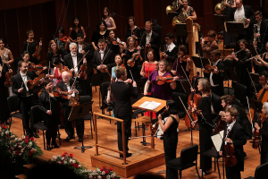 Photo depicting Indianapolis symphony orchestra during an opening night gala. Conductor is in the middle of the photo, everyone else has their instruments in hand.