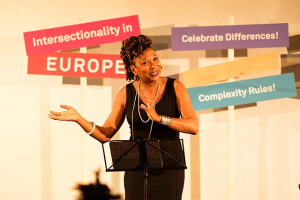 Image of Kimberle Crenshaw speaking in about intersectionlity in Germancy. Visuals behind her say "Intersectionality in Europe" "Celebrete Difference" and "Complexity Rules!"