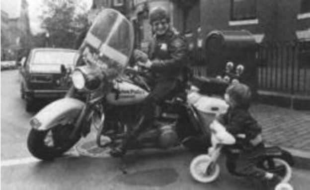 A policeman on a motorbike looking at a child who is sitting on a bicycle beside the policeman.