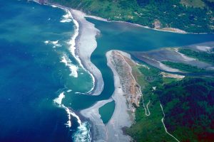 A photograph of an estuary where a sand bar separates the ocean from the mouth of the river.