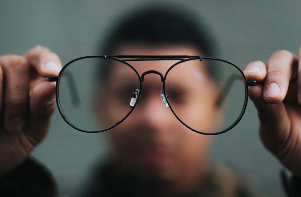 A dark-skinned person slightly out of focus peering through wire-rimmed glasses.