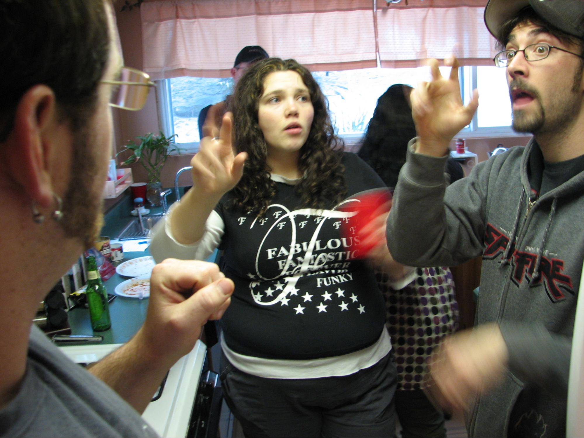 Three deaf adults stand in a kitchen having a conversation in ASL.