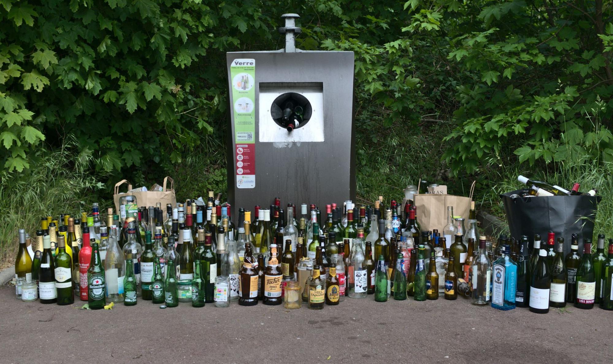 an enormous collection of wine bottles, beer bottles, cans, water bottles and other beverage containers in front of a recycling bottle deposit box.
