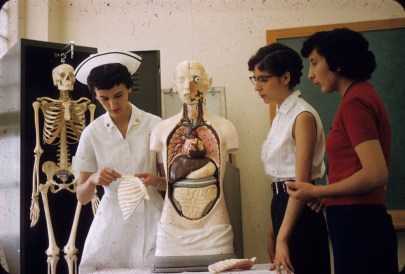 Three indigenous women stand around an anatomical model. One woman wears a nurses uniform.