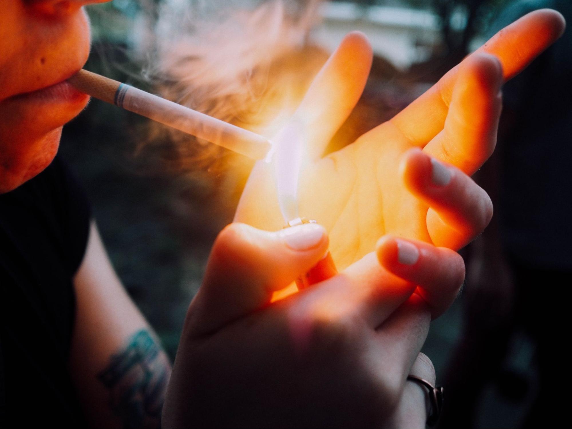 Person lighting a cigarette. The cigarette and the flame are the focus of the picture.