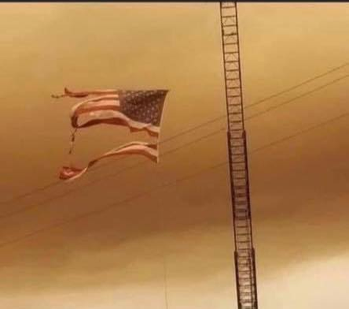 Fire-damaged flag blowing in wind in a smoky sky