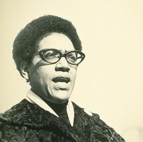 Audre Lorde, black woman activist and poet, has an afro and wears black framed glasses.