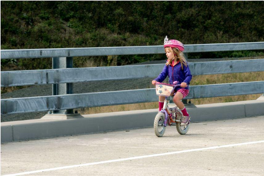 Young child riding small two wheeled bike across bridge by roadway