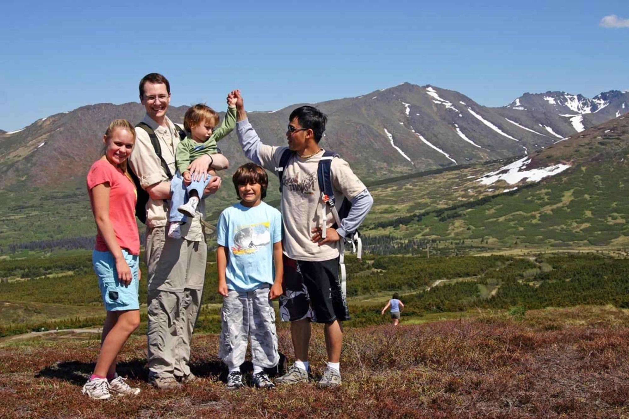 An adult man with four children standing in front of mountain, various ethnicities