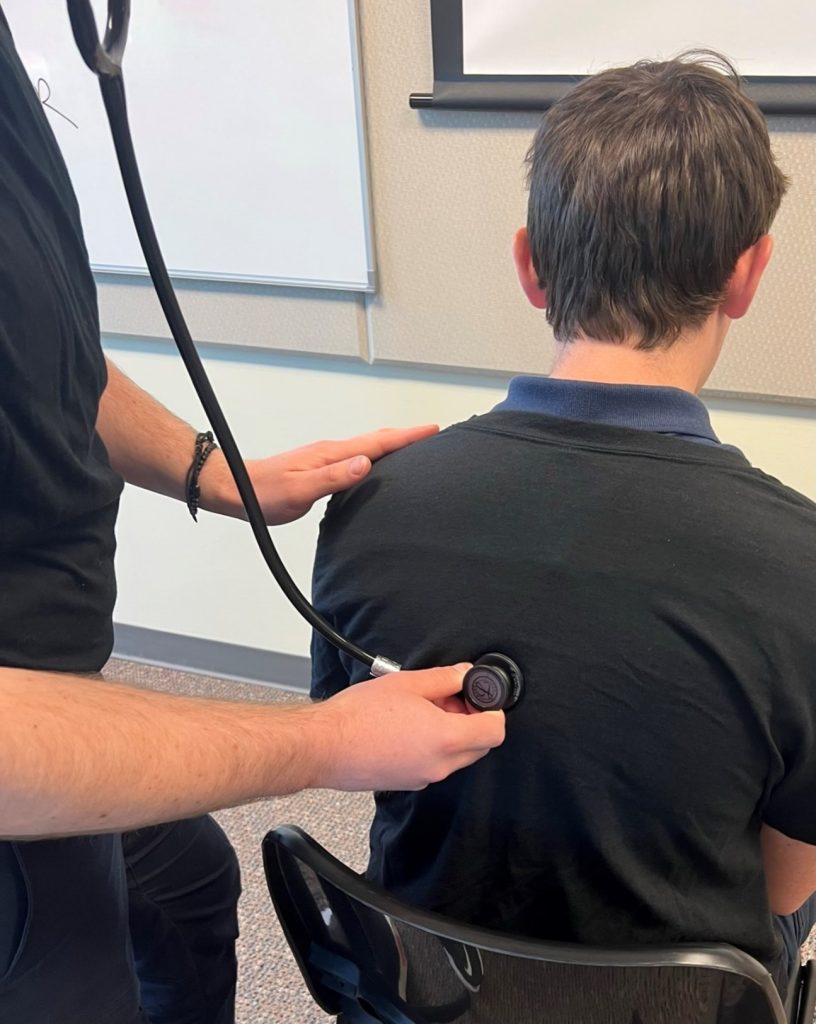 A person using a stethoscope to listen to a patient's right posterior lower lung.